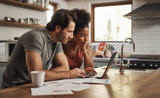 Cropped shot of a couple using their laptop and going through paperwork at home